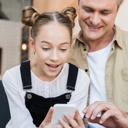 A parent and child smiling together while looking at a phone